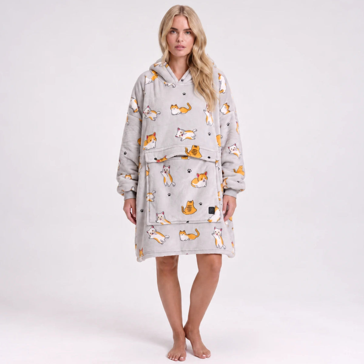 A woman stands barefoot against a light gray studio background wearing a Solrevé Solis™  hooded fleece robe with an allover print of orange and white cats and small gray stars.